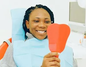 A woman is sitting in a dental chair holding a red heart shaped mirror.