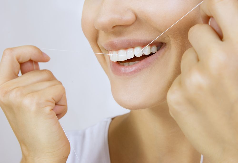 A woman is flossing her teeth with a dental floss.