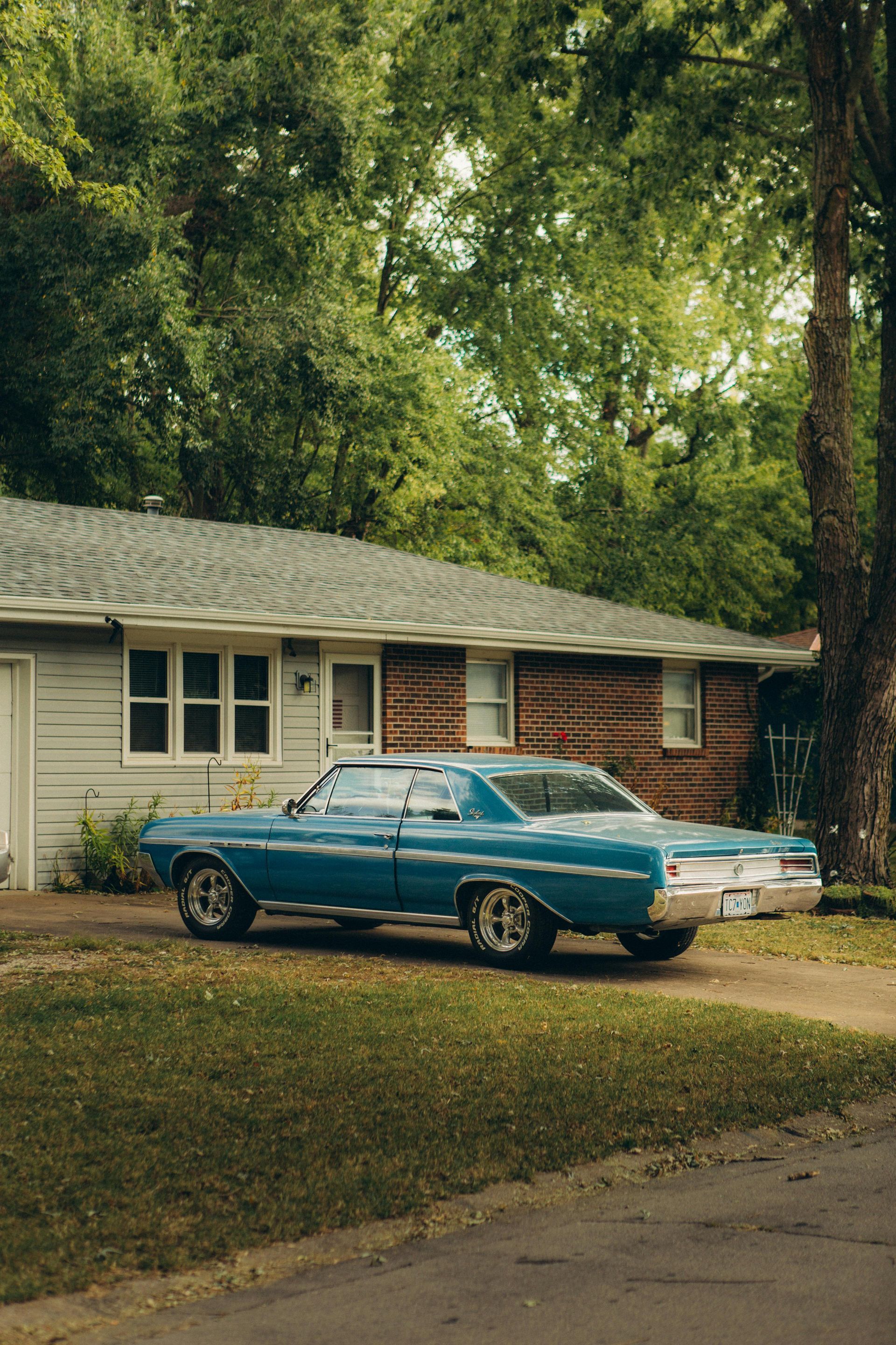 A blue car is parked in front of a brick house.