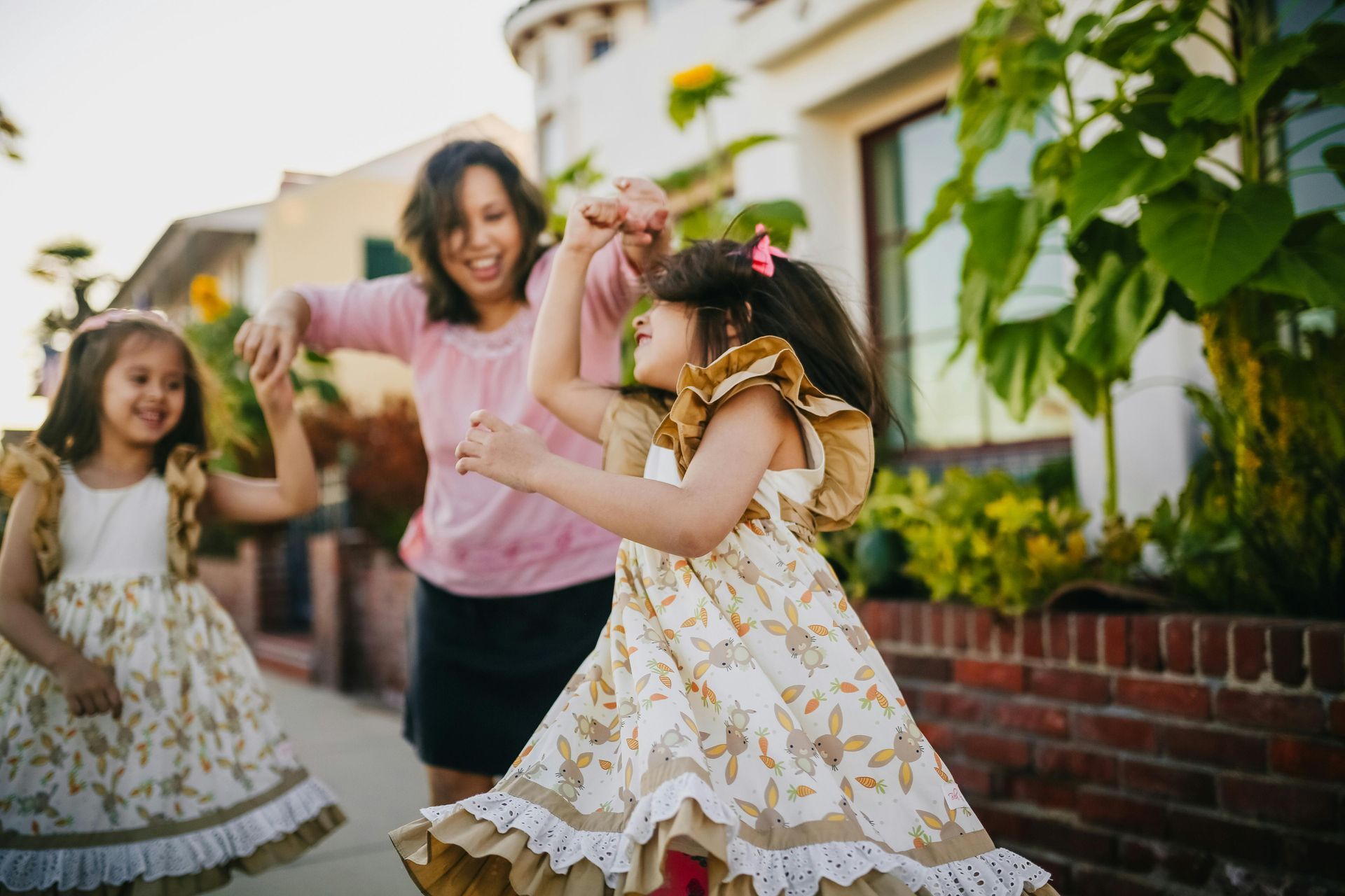 A woman and two little girls are dancing on the sidewalk.