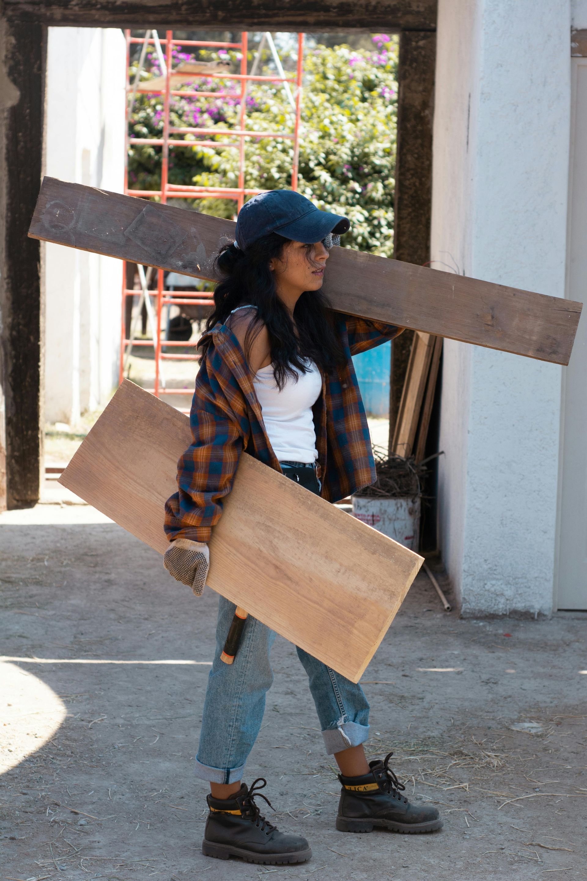 A woman is carrying a large piece of wood over her shoulder.