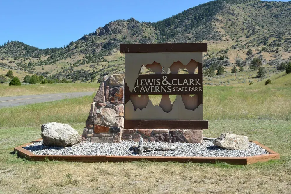 Lewis & Clark Caverns State Park sign on a grassy roadside with mountains in the background
