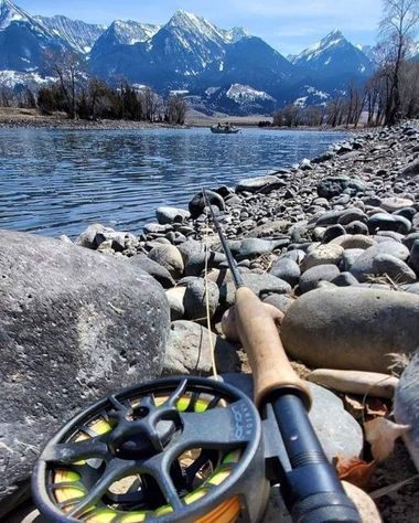 Fly fishing rod and reel on a rocky lakeshore with snowy mountains and blue water in the background