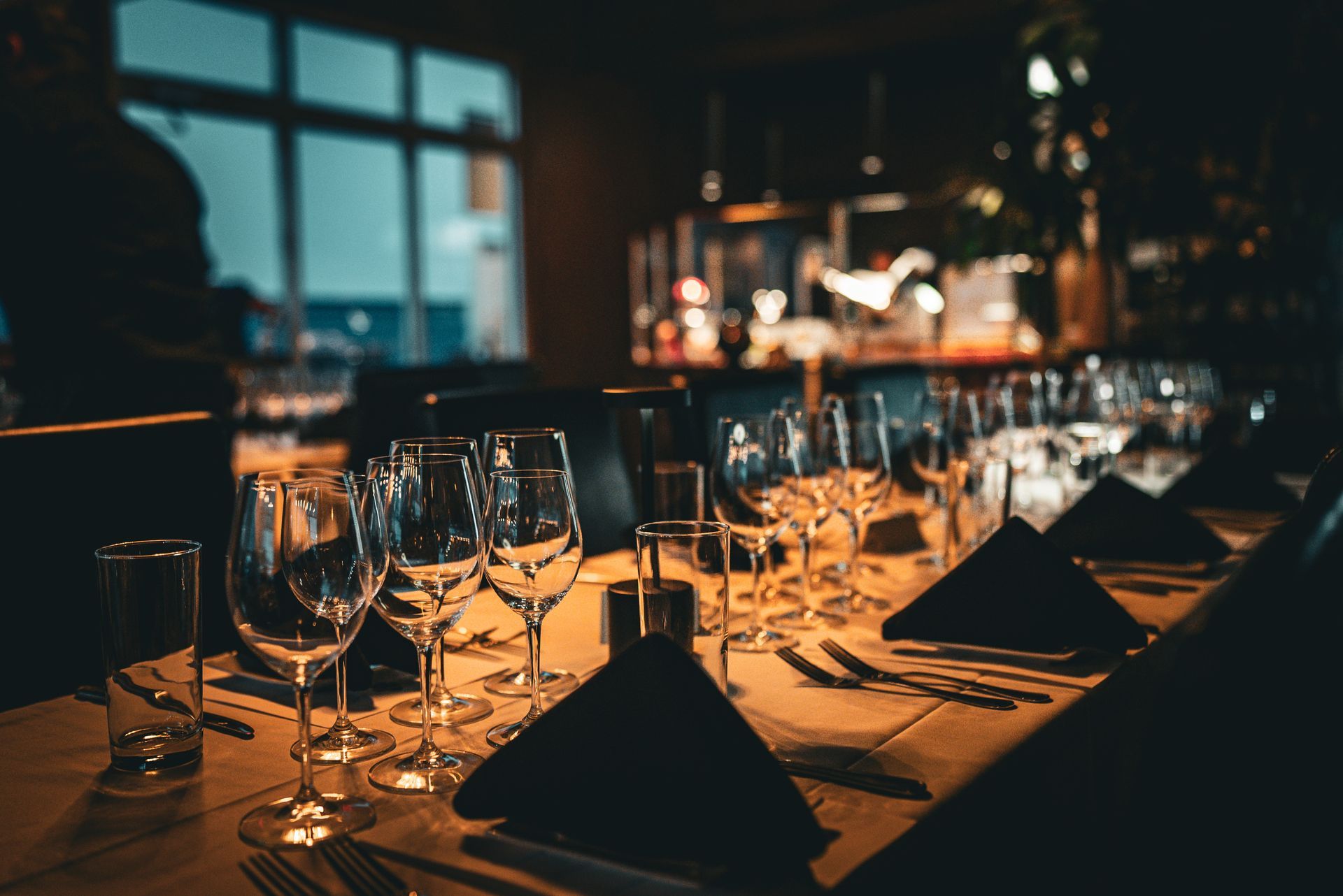 Formal dining table set with glasses, napkins, and silverware, in a dimly lit restaurant setting.