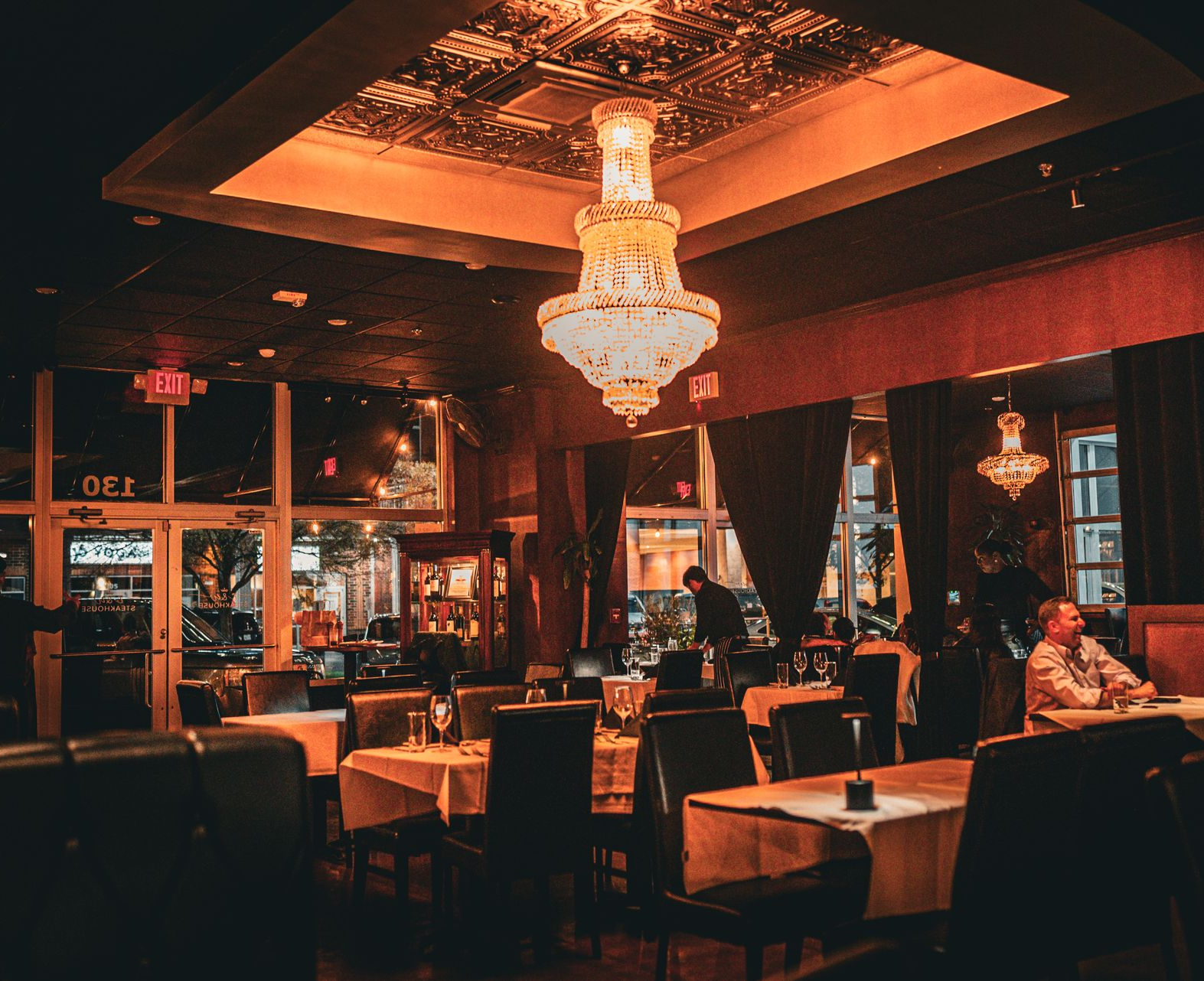 Dimly lit restaurant interior with tables set for dining and a large chandelier.