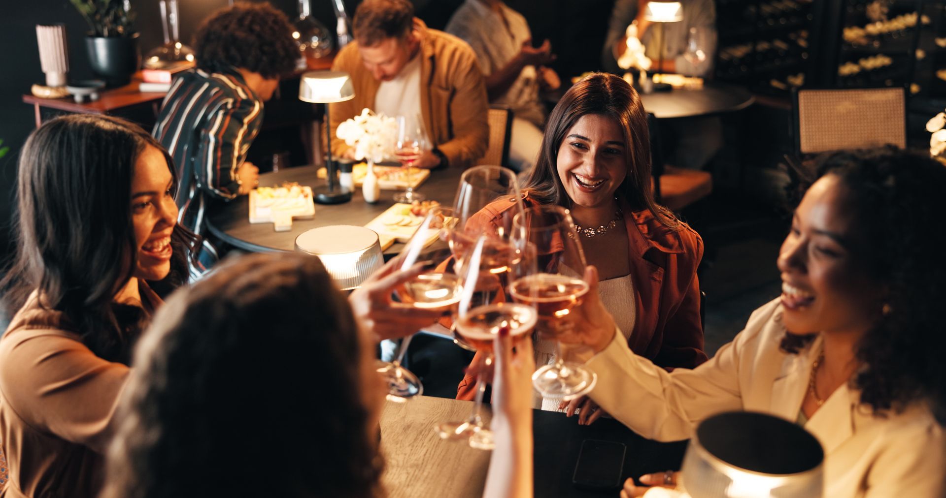 Group of people toasting with rose wine at a restaurant table, smiling and enjoying a meal.