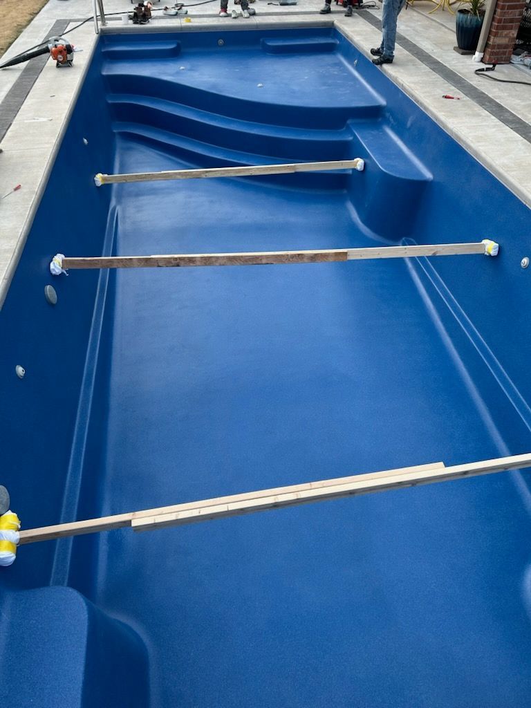 Blue swimming pool under construction; metal bars extend across the pool; workers in the background.