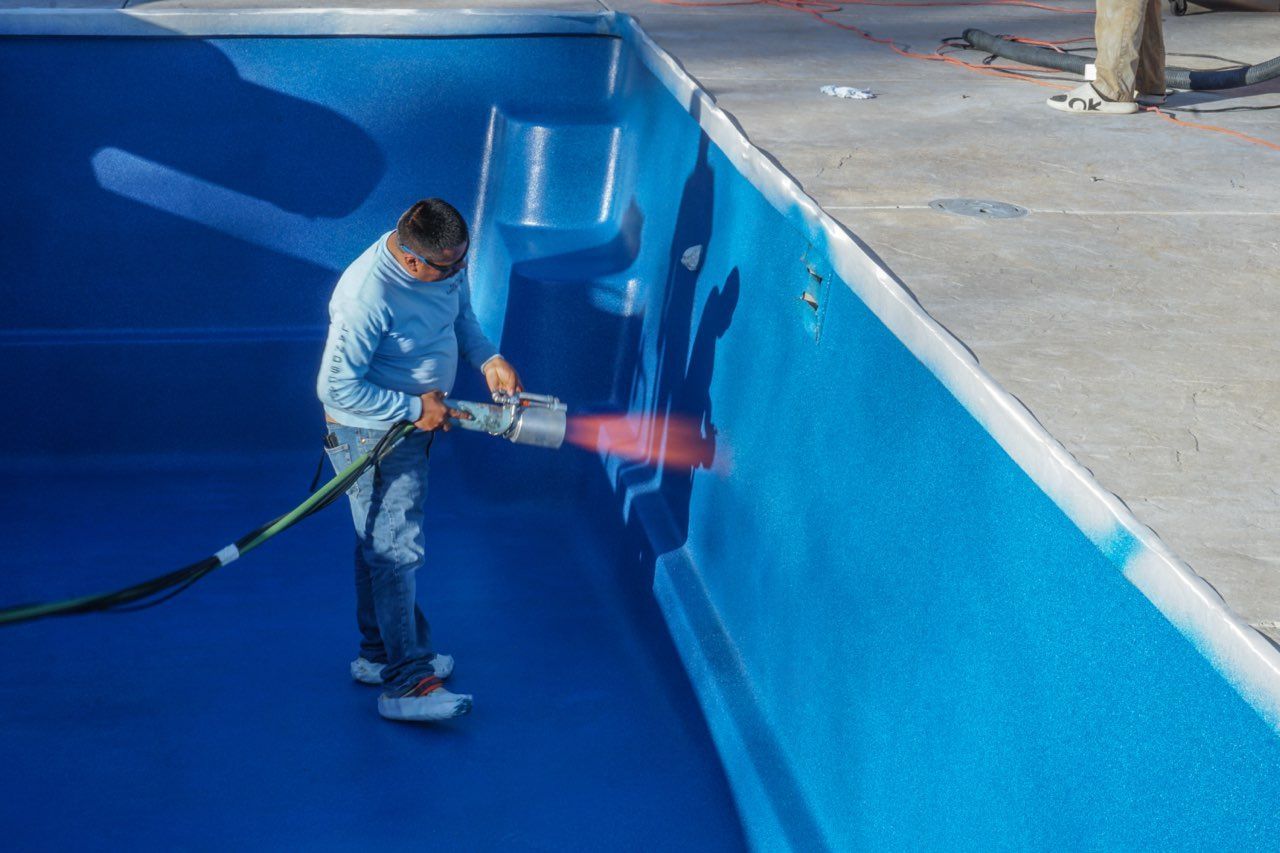 Person spraying coating inside a blue pool. White trim, blue walls and floor.