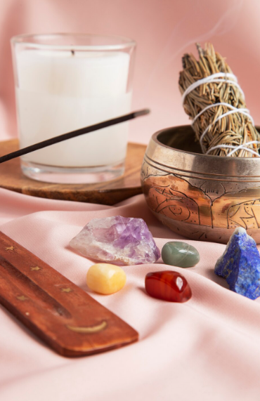 Vela, incienso, cristales y un manojo de hierbas aromáticas dispuestos sobre una tela rosa