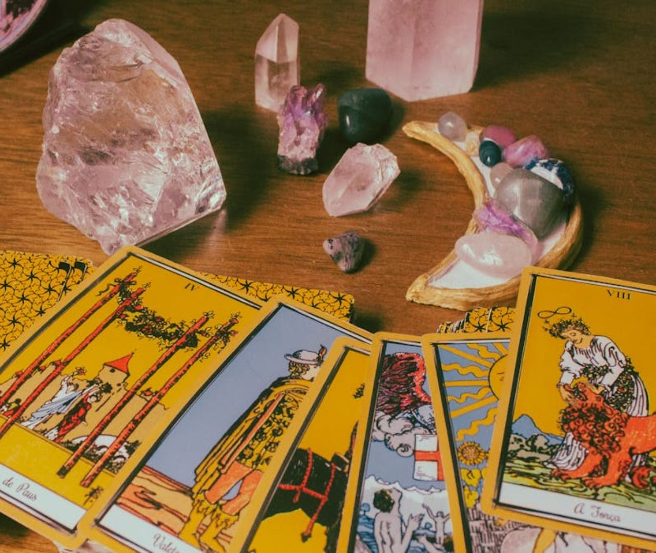 Cartas del tarot y cristales sobre una mesa de madera, entre ellos un cuarzo rosa, una amatista y pequeñas piedras pulidas.