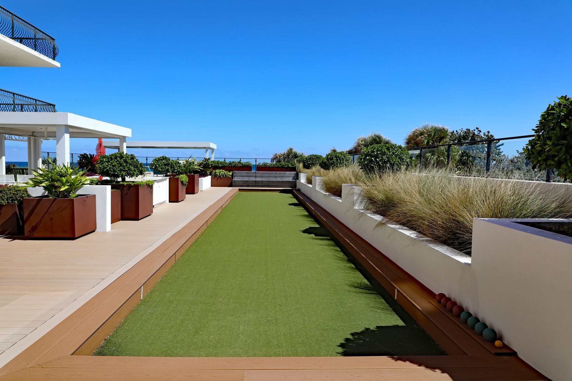 A bocce ball court on a rooftop with ocean view and blue sky. Green turf and wooden trim.