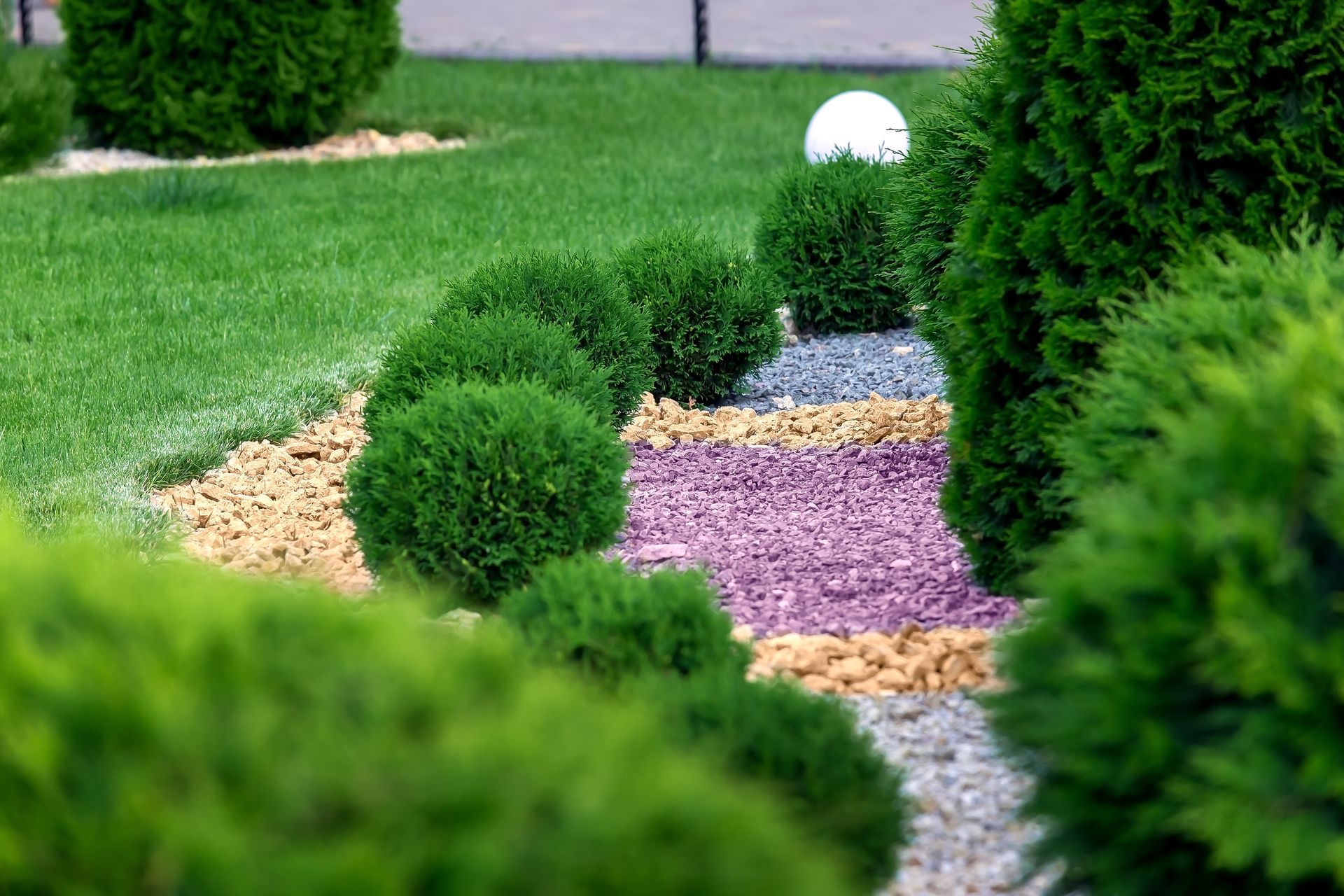 Green manicured garden with spherical shrubs, gravel pathways of various colors.