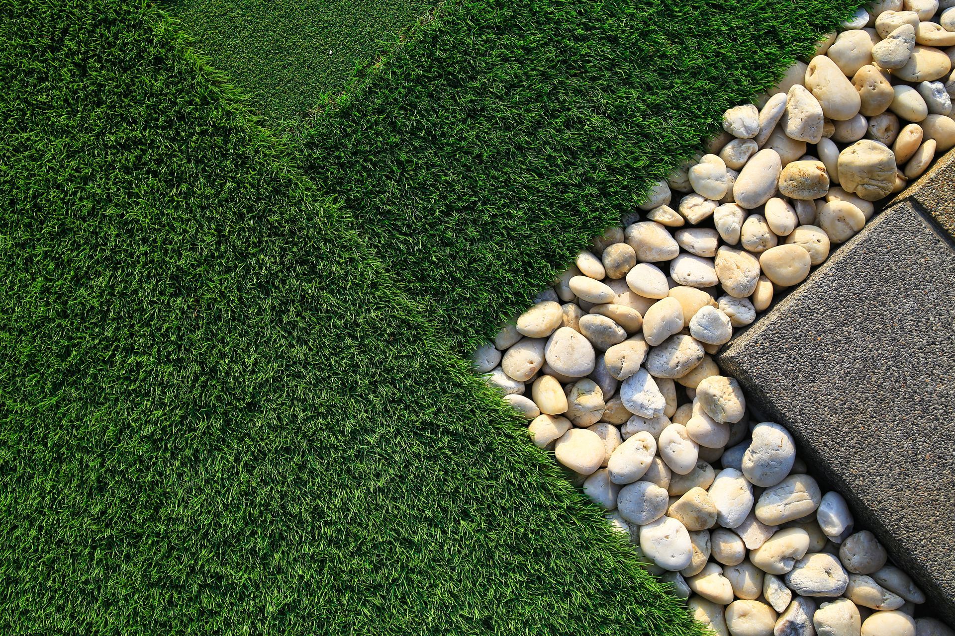 Green artificial grass with white pebbles and gray paving stones.