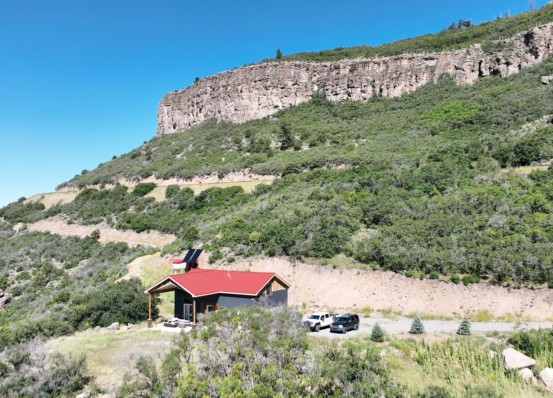 A small house with a red roof is sitting on top of a hill surrounded by trees. Maven Construction, Montrose, CO