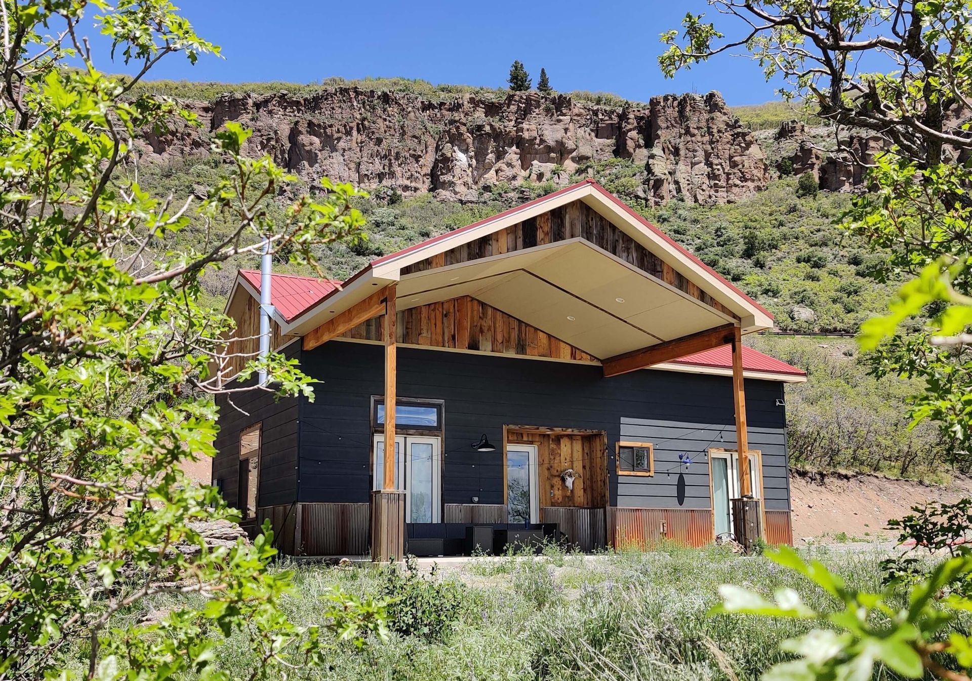 A black house with a red roof is surrounded by trees and grass. Maven Construction, Montrose, CO