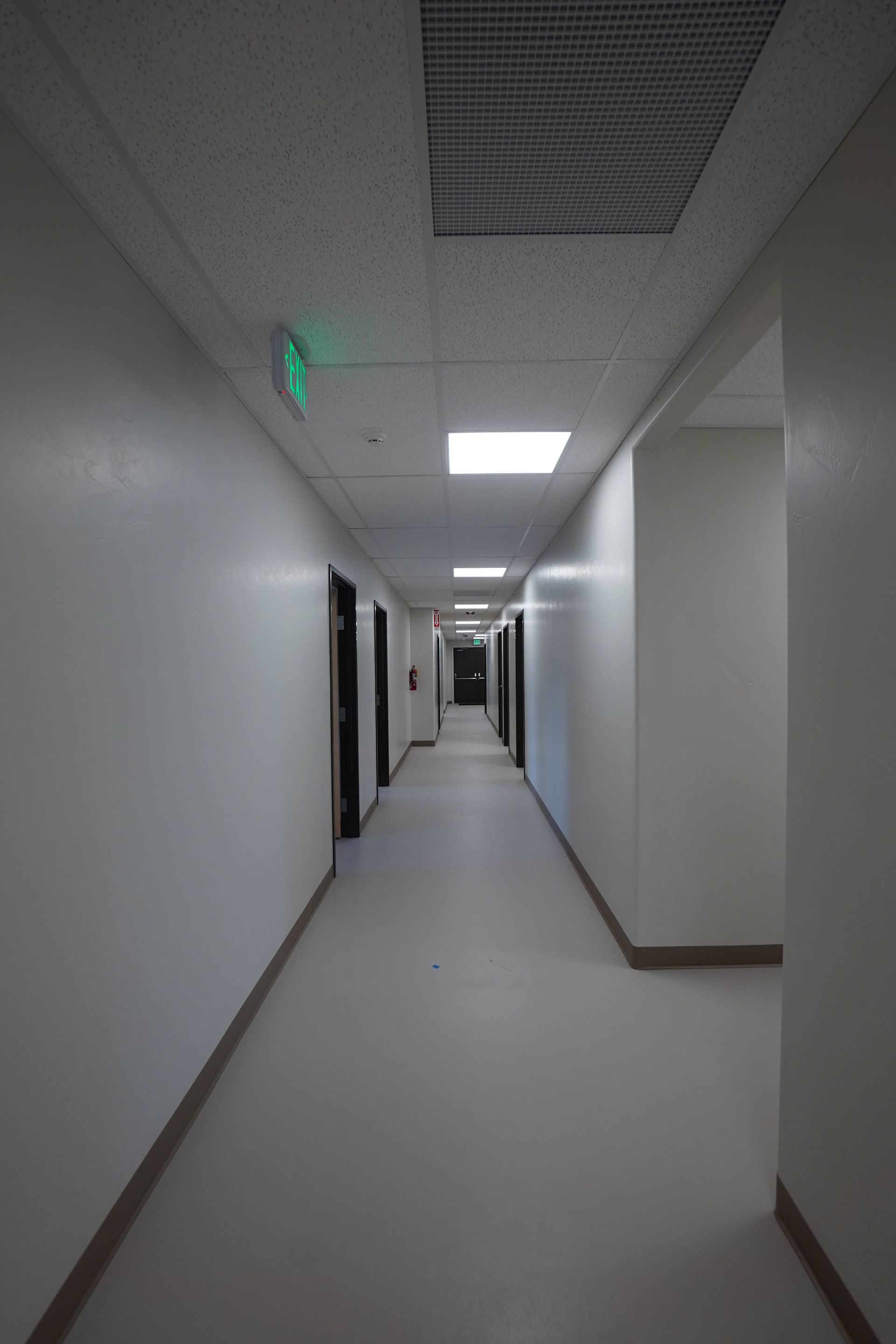 A long hallway in a building with a green exit sign on the ceiling. Maven Construction, Montrose, CO