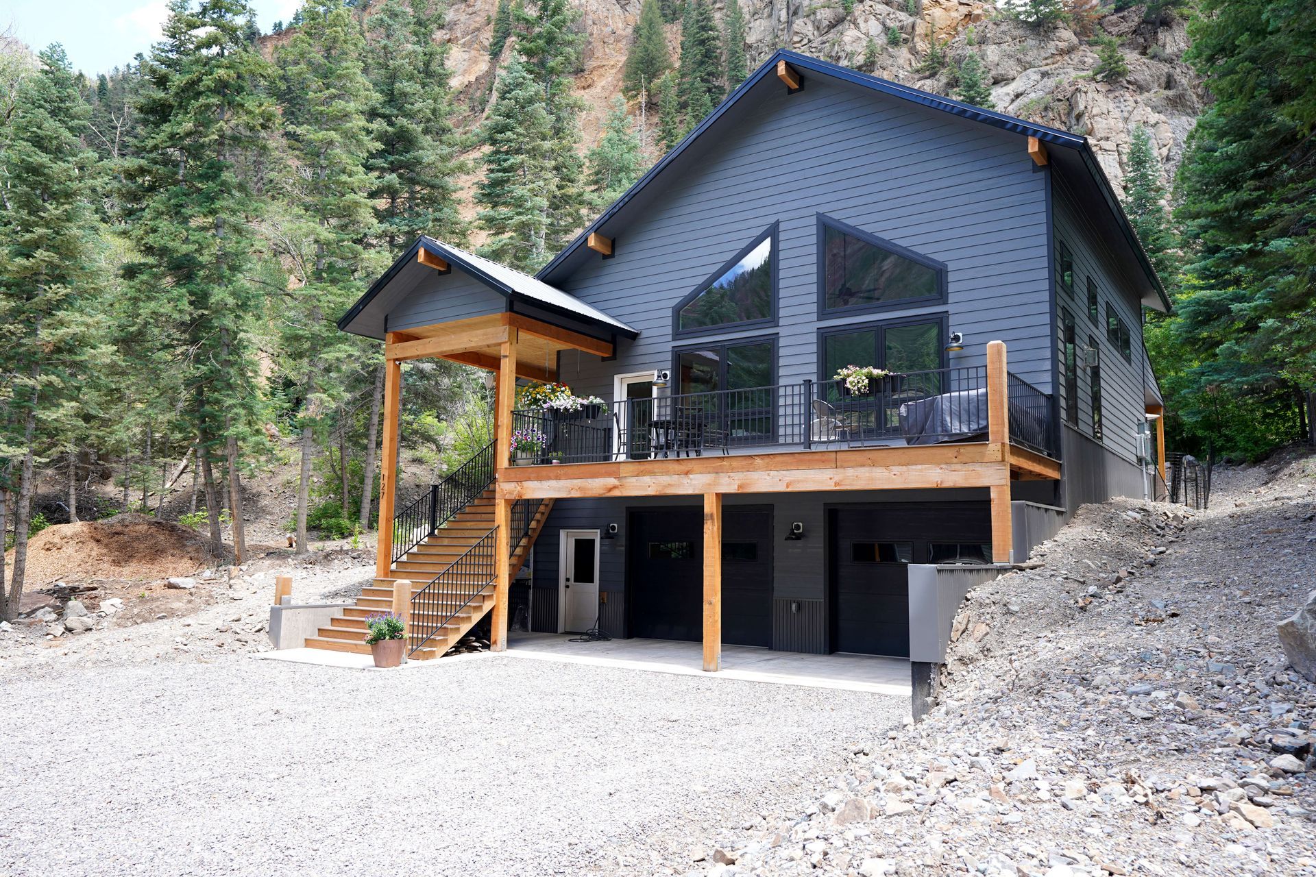 A large gray house with a large deck in the middle of a forest Maven Construction, Montrose, CO