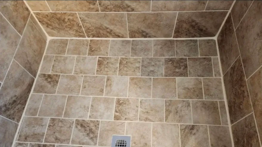 Shower stall with brown square tiles and white grout.