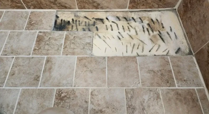 Damaged bathroom floor tiles. The center section is removed, showing black marks. Brown and tan tiles.