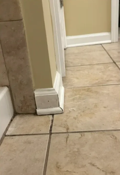 Baseboard molding where wall meets floor tile. Beige tile and light beige paint visible.