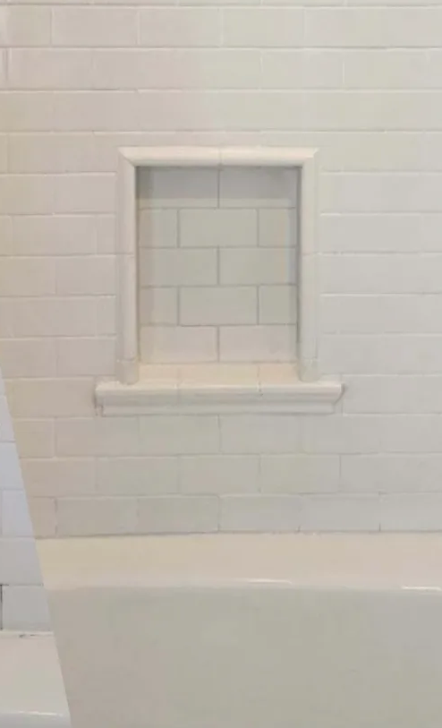 White tiled bathroom with built-in shelf above a bathtub.