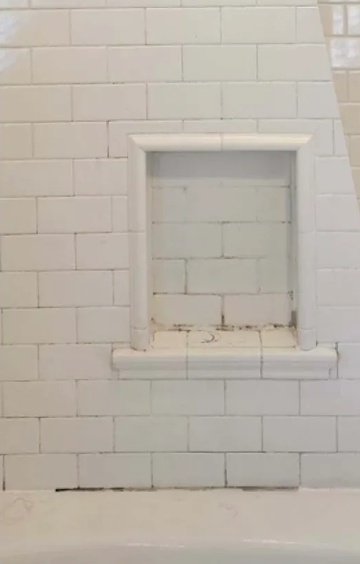 White tiled bathroom wall with built-in shelf.