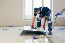 Person installing floor tiles with tools in a room with a window.