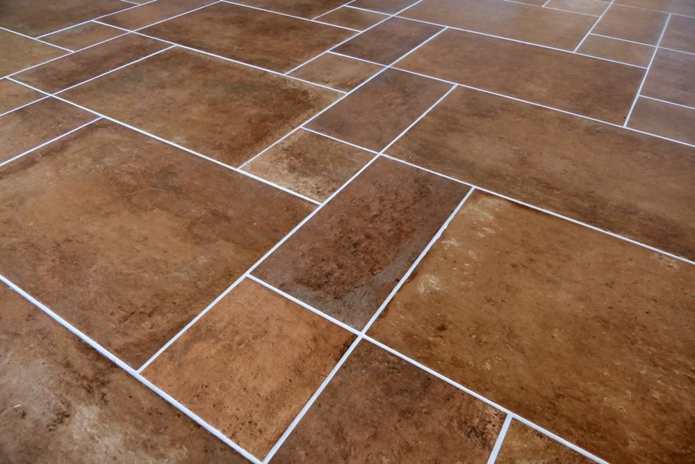 Brown ceramic tile floor with white grout in a random pattern.