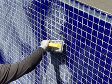 Person grouting blue tile on a pool wall using a yellow float tool.