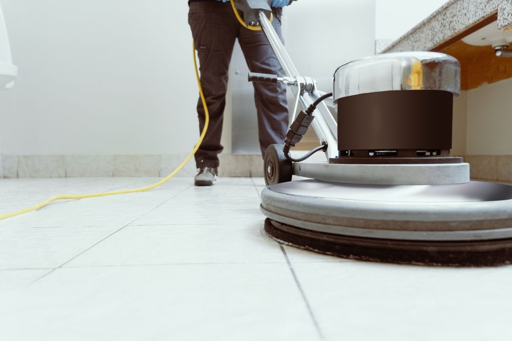 Person using a floor buffer to clean a tiled floor; yellow power cord.