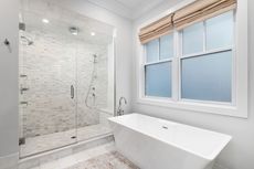 Modern bathroom with glass shower, freestanding tub, and window with shade.