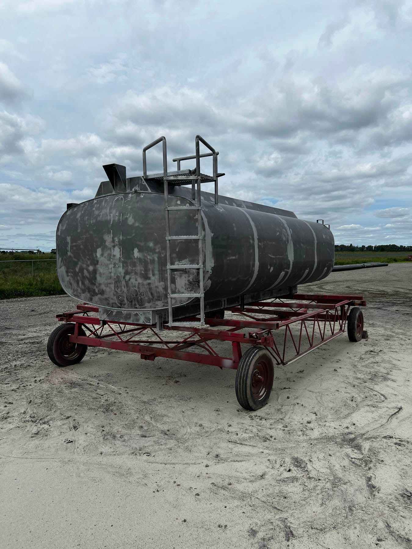 Large, dark, cylindrical tank on a red trailer, with a ladder on top. Set in a sandy, outdoor location.