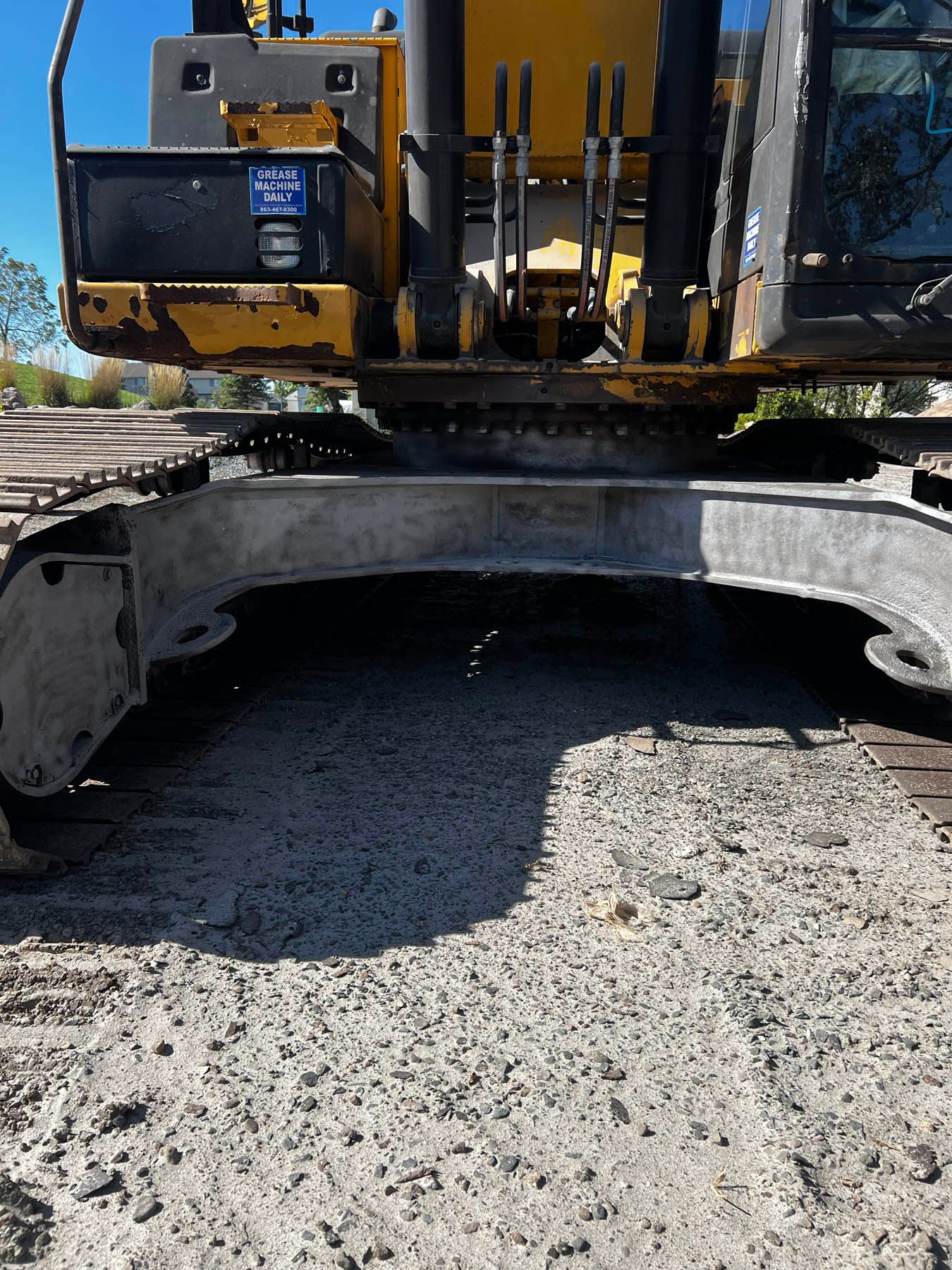 Close-up of a yellow and black excavator's undercarriage resting on a surface of gray gravel.