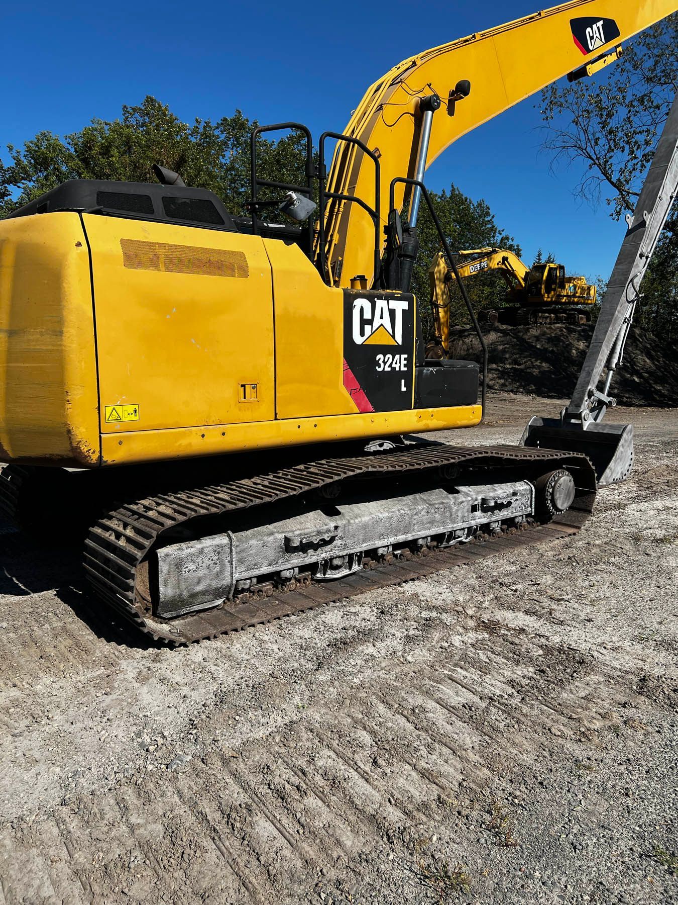 Yellow Caterpillar 326E excavator on a gravel surface, under a blue sky.