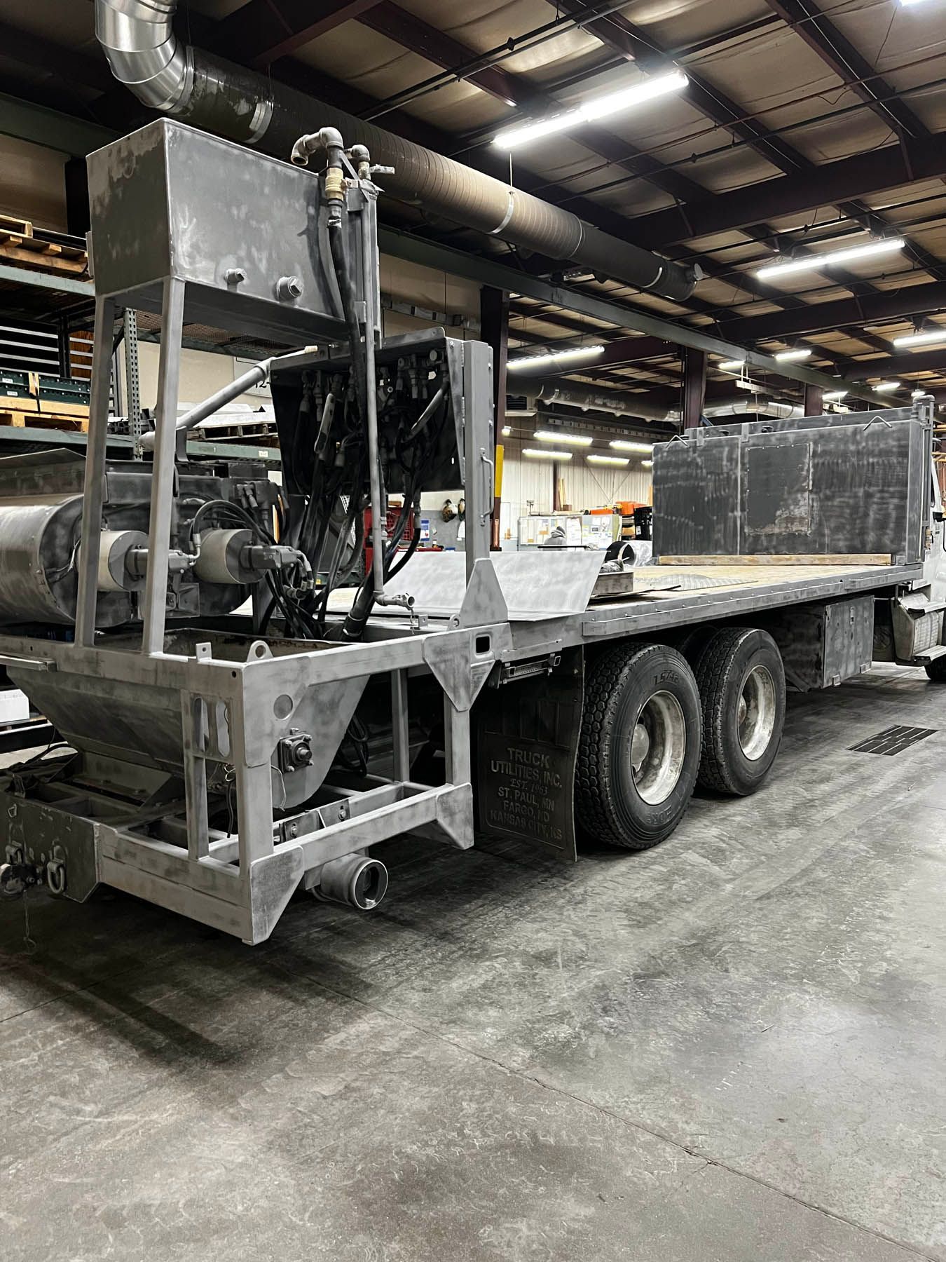 A flatbed truck with equipment, likely for industrial use, inside a warehouse. The truck is metallic, with multiple tanks and machinery.
