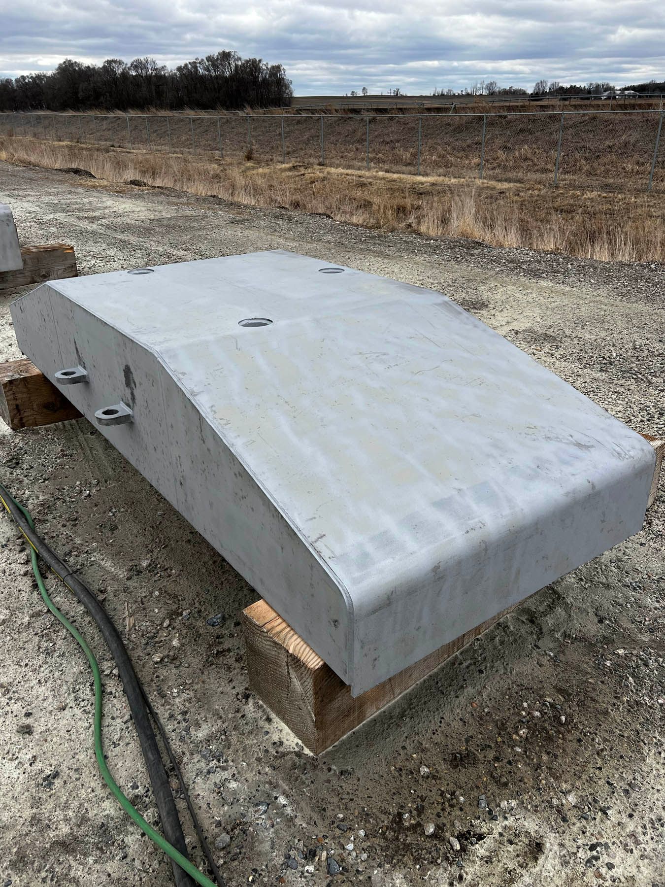 A large, curved concrete block resting on wooden supports, outdoors on a construction site.