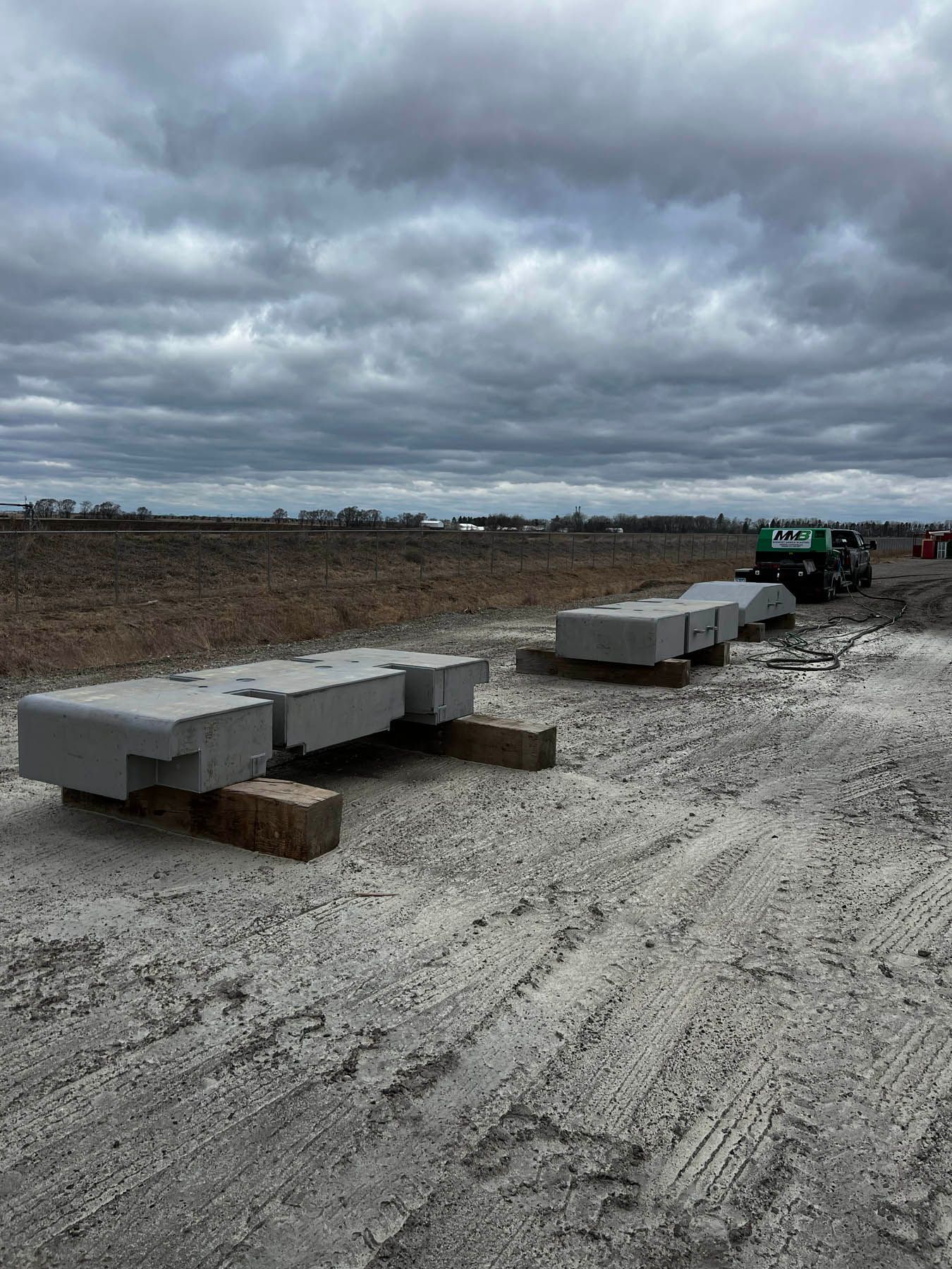 Concrete blocks on wooden supports at a construction site under a cloudy sky. Dirt and machinery are also visible.