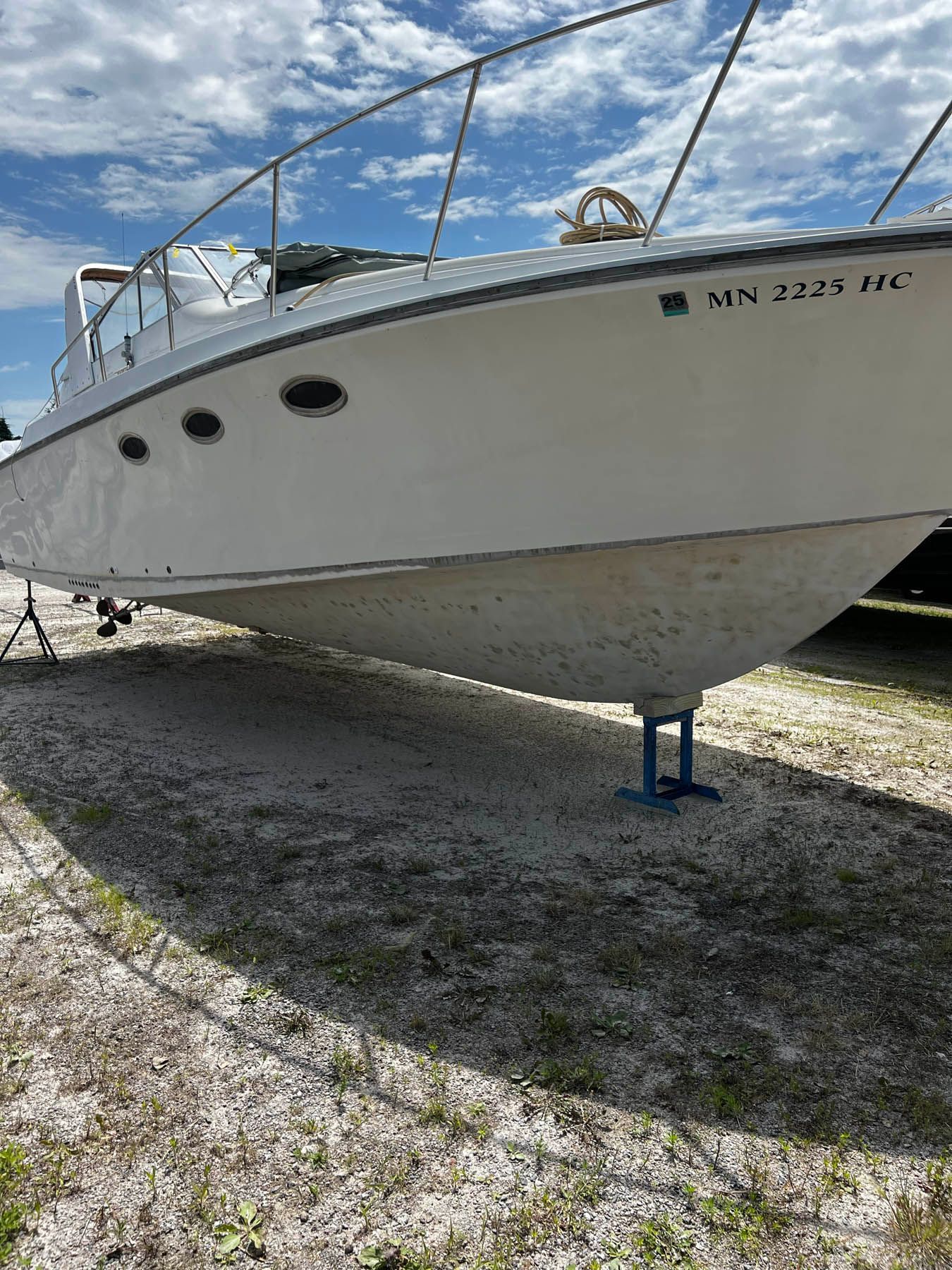 White boat on blocks, outside on gravel. Its hull has visible barnacles. Minnesota registration numbers on side.