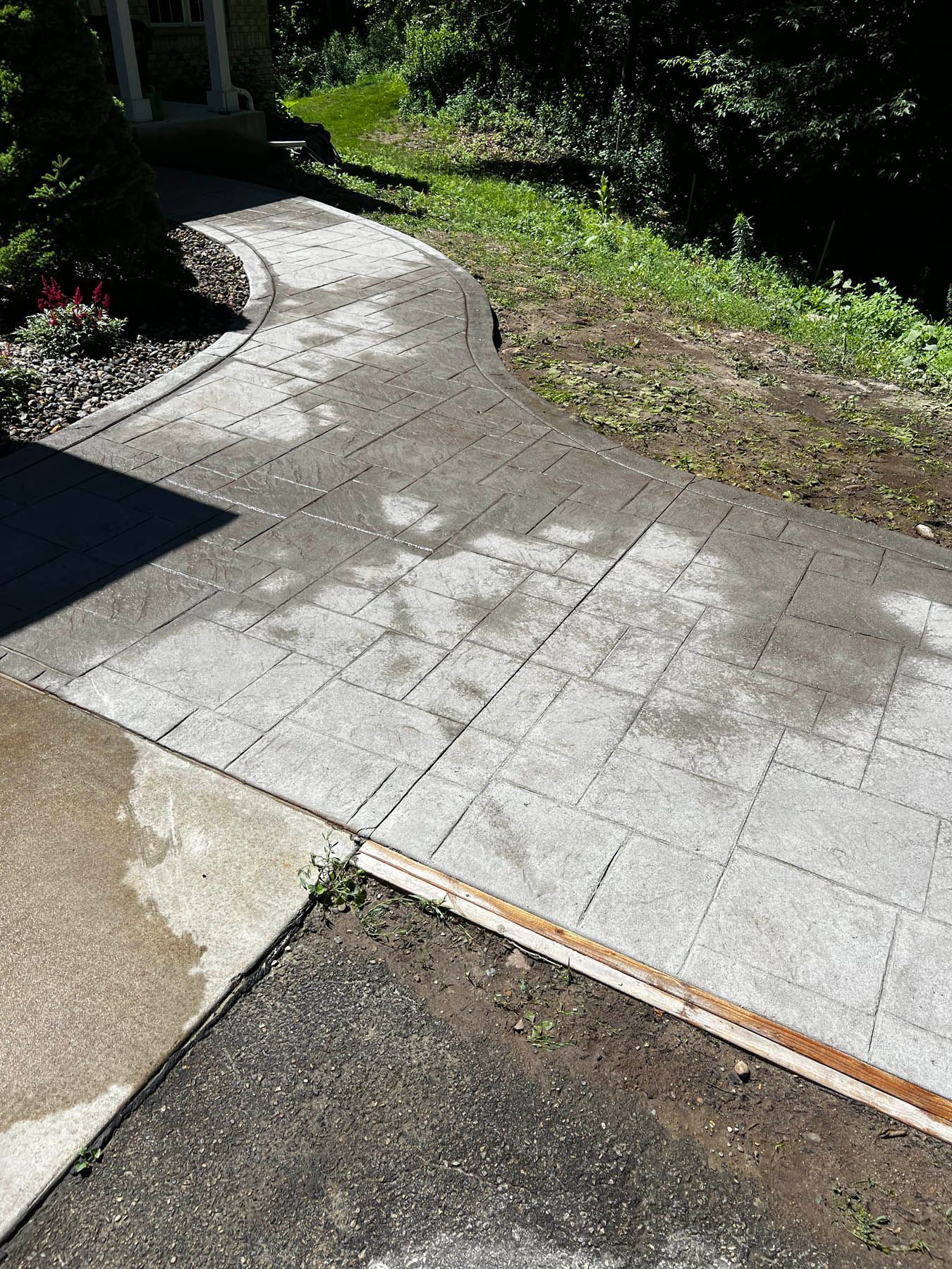 Gray brick walkway leading to a house entrance. Patches of lighter color indicate possible cleaning.