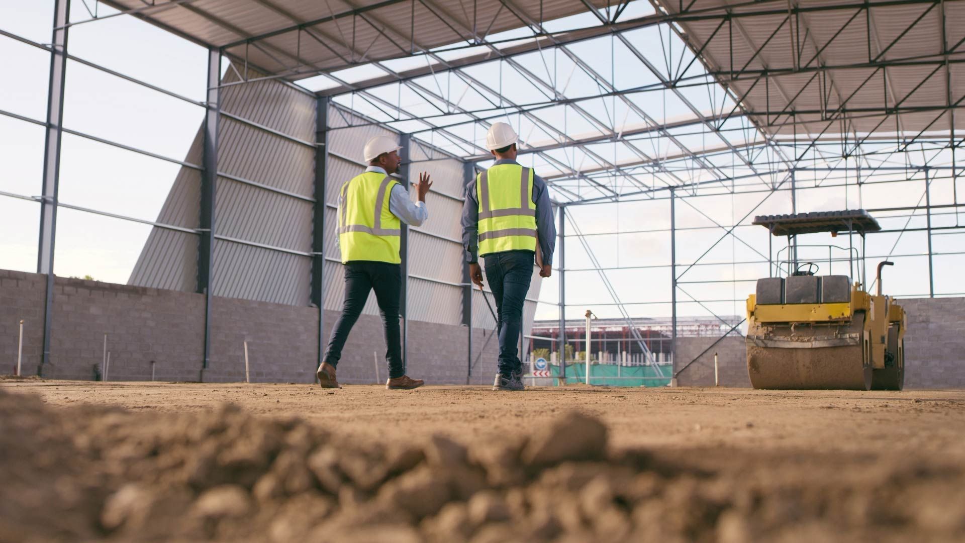 Two construction workers are walking through a building under construction.