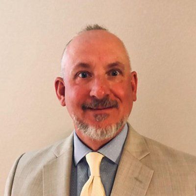 Middle-aged man with short hair and goatee in a light suit and tie smiles at the camera.