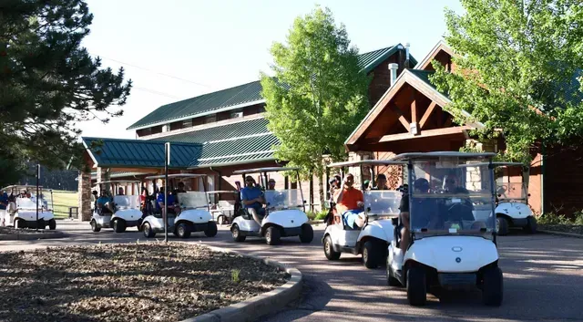 Golf carts lined up in front of a lodge-style building, likely at a golf course.