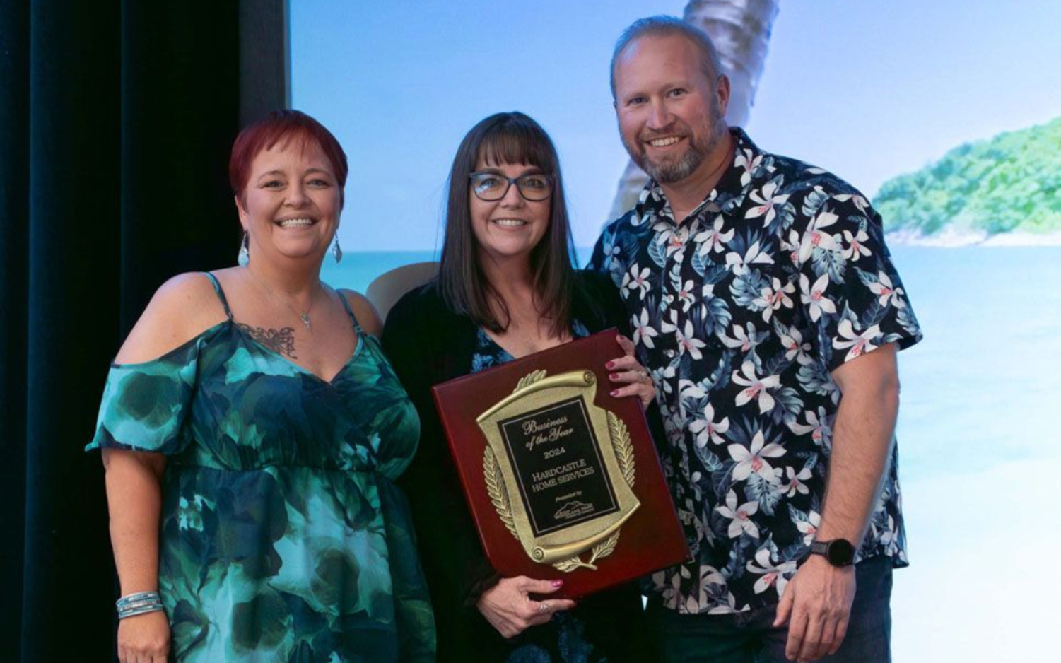 Two men on stage, one holding an award. Dark suit, plaid jacket, dark curtains.