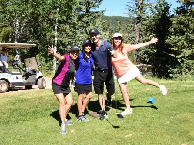 Four people pose on a golf course. Two women smile and the man in the middle smiles. Green grass, trees.