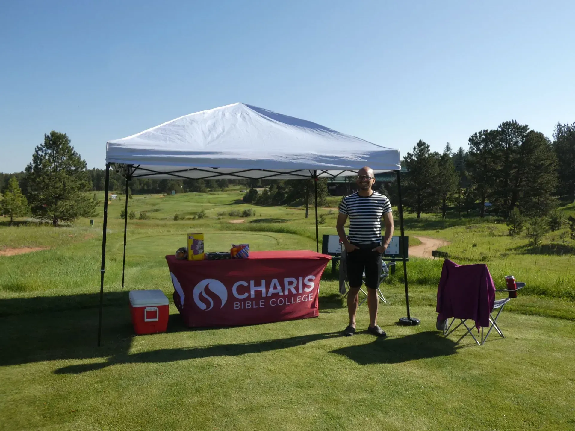 Man stands by a table under a white tent, in a golf course, with a logo that says