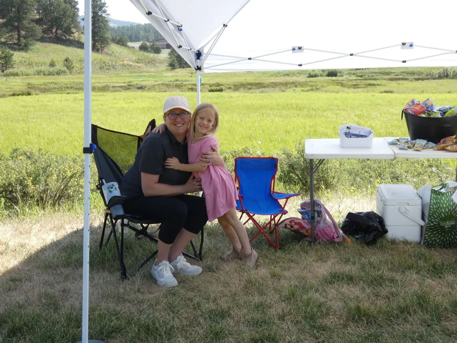 Woman and girl hugging under a white canopy in a field.