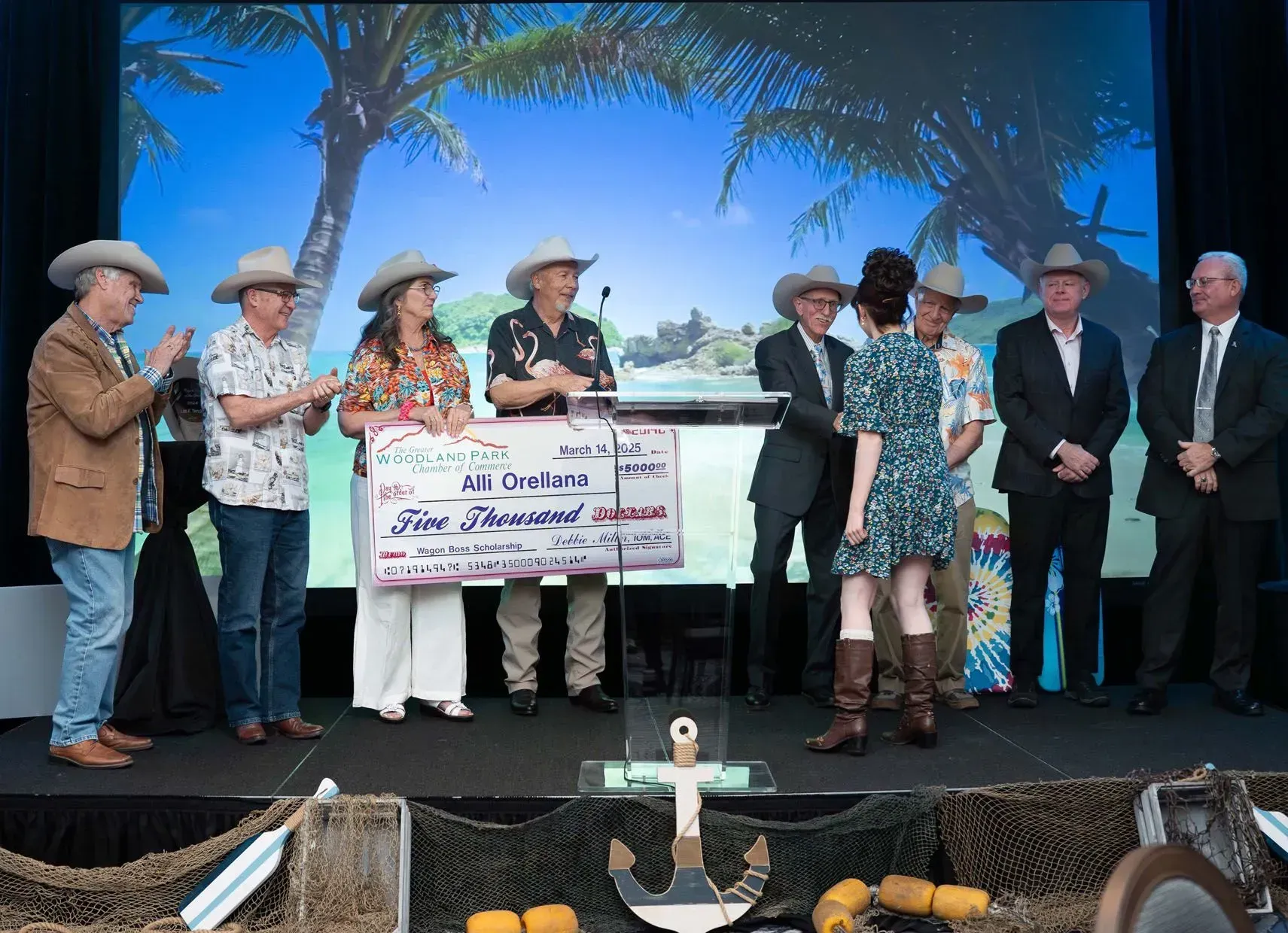 People in cowboy hats present a large check to a woman onstage with a tropical backdrop.