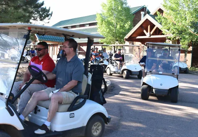 Men in golf carts lined up outdoors, preparing to play golf.