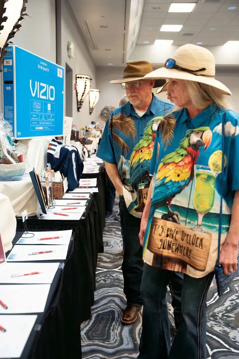 Couple in matching parrot shirts and hats, browsing items at a silent auction.