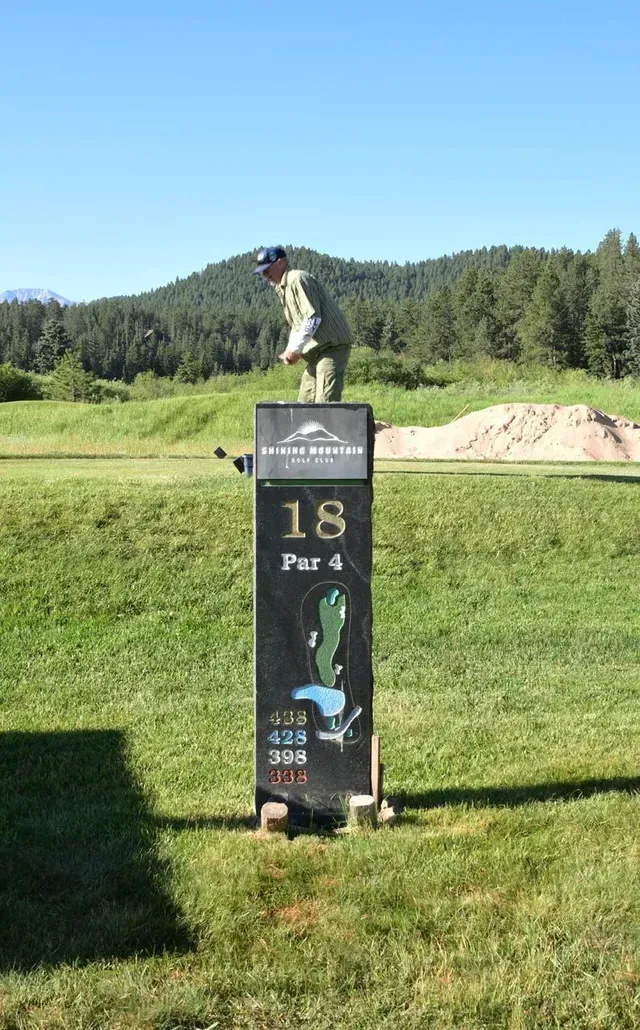 Golfer teeing off on the 18th hole of a golf course. Sign shows Par 4 with map of the hole.